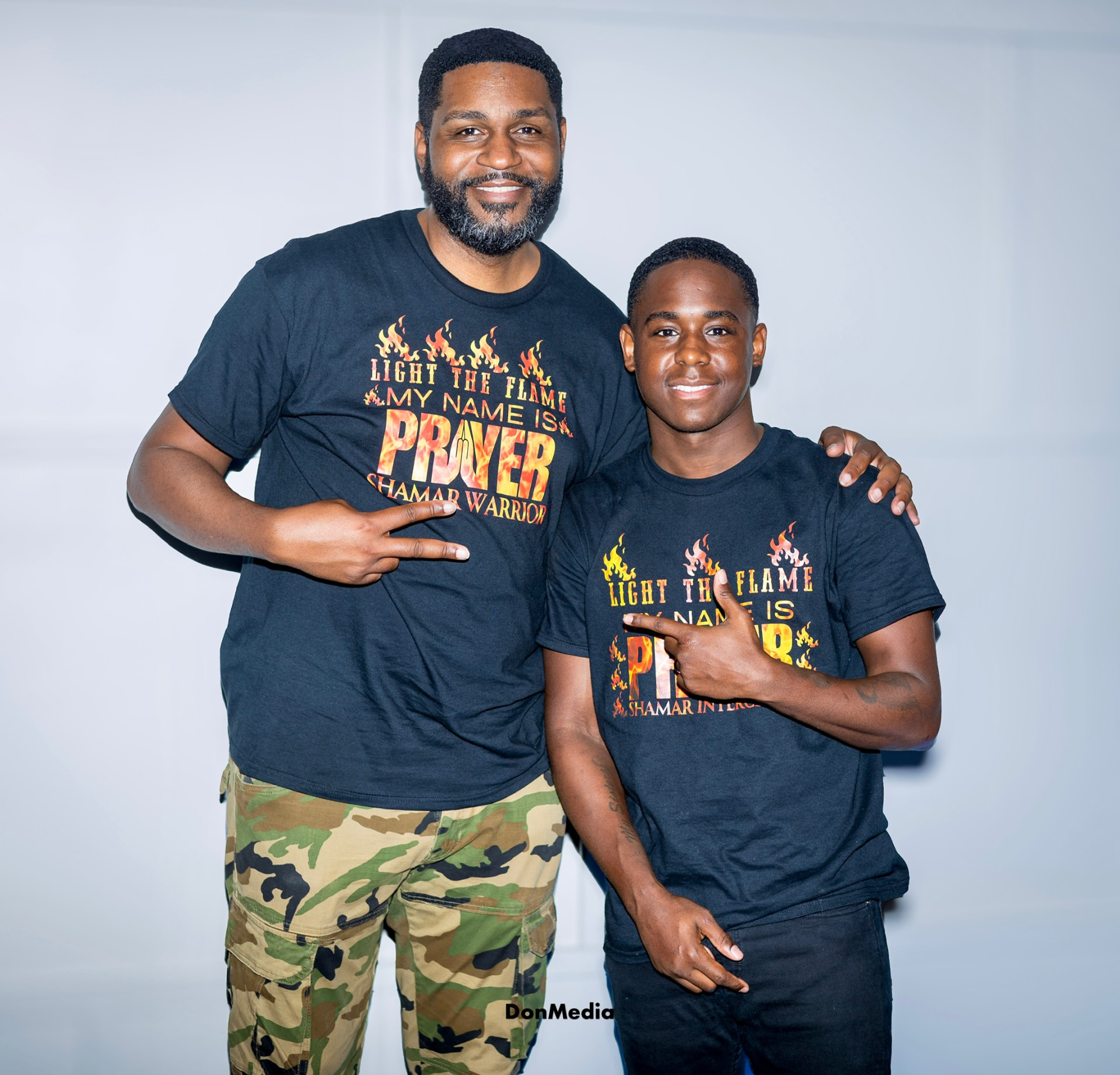 A father and son wearing black Light The Flame My Name Is Prayer tees