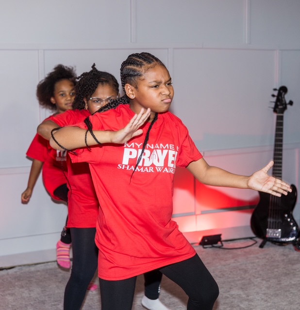 Young dancers wearing red My Name Is Prayer Shamar Warrior tees