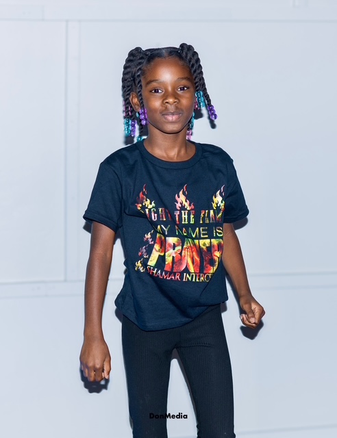 A young girl wearing the black Light The Flame My Name Is Prayer tee